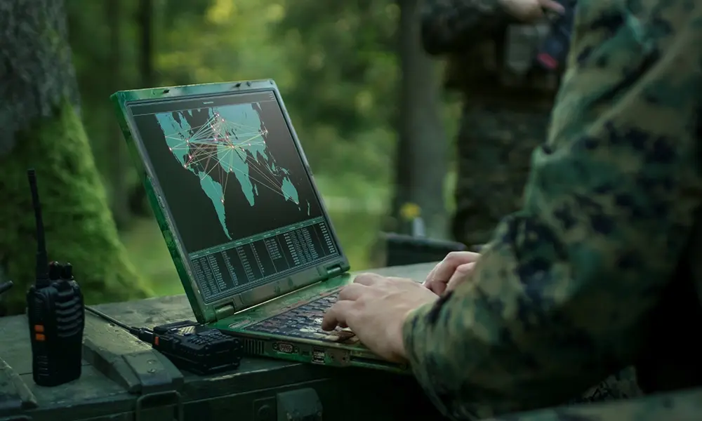 A military technologist views a map on a laptop outdoors. 